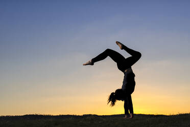Young woman in silhouette doing handstand during sunset - STSF02890