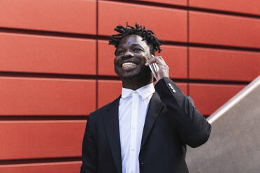 Happy mid adult businessman talking on mobile phone in front of red wall - PNAF01010