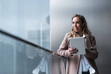 Smiling businesswoman holding digital tablet while looking away against wall - JMPF00894
