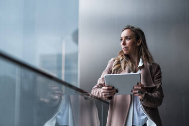 Female entrepreneur day dreaming while holding digital tablet in front of gray wall - JMPF00895