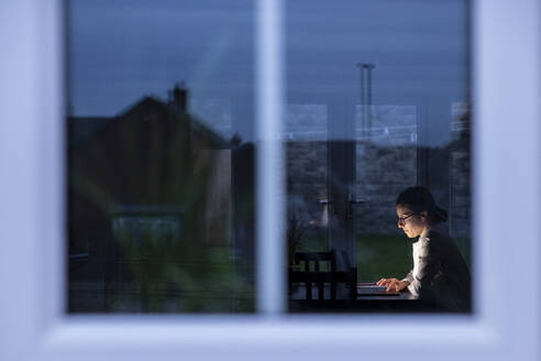 Unternehmerin bei der Arbeit mit Laptop in der Nacht durch ein Fenster gesehen - WPEF04230