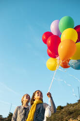 Cheerful girls playing with colorful helium balloons - LJF02164