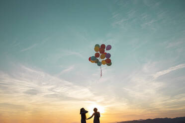 Mädchen in Silhouette Blick auf Helium-Ballons fliegen in der Luft während des Sonnenuntergangs - LJF02166