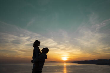 Father in silhouette carrying daughter during sunset - LJF02167