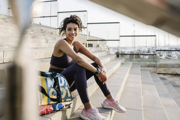 Lächelnde Sportlerin, die mit einer Tasche auf einer Treppe sitzt und träumt - XLGF01361