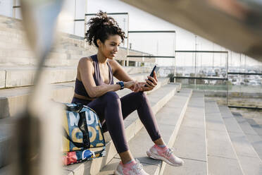 Eine Sportlerin benutzt ein Mobiltelefon, während sie auf einer Treppe sitzt - XLGF01362