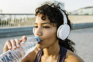 Erwachsene Sportlerin mit Kopfhörern, die Wasser aus einer Flasche trinkt - XLGF01370