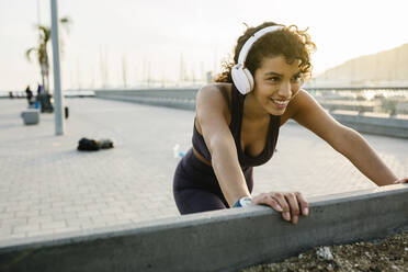 Smiling sportswoman listening music through headphones while exercising on bridge - XLGF01372