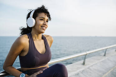 Nachdenkliche Sportlerin mit Kopfhörern auf einer Brücke sitzend - XLGF01377