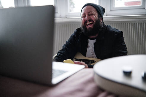 Mature man with laptop laughing at home - ASGF00083