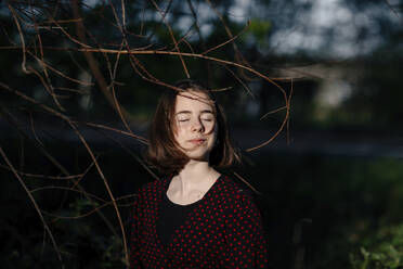 Mädchen mit geschlossenen Augen an einem kahlen Baum stehend - OGF00990