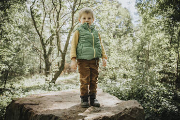 Cute boy standing on boulder in forest - MFF07660
