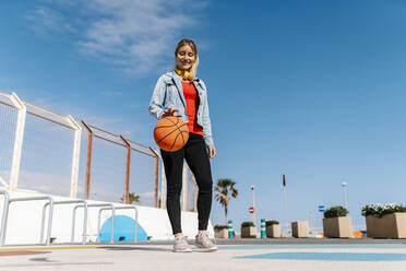 Lächelnde Frau spielt mit Basketball auf dem Boden gegen den Himmel - EGAF02078