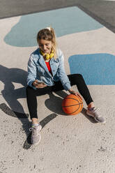 Frau mit Basketball, die ihr Smartphone benutzt, während sie auf dem Boden sitzt - EGAF02080