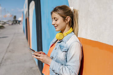 Blonde Frau mit Smartphone an der Wand - EGAF02083