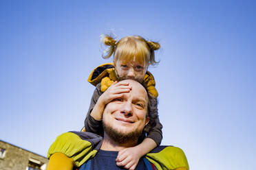 Smiling man piggybacking blond daughter against sky - IHF00421