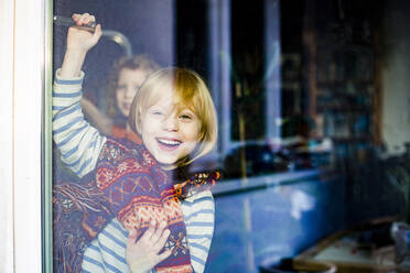 Cheerful girl with brother seen through glass door - IHF00433