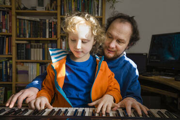 Father teaching synthesizer to son while at home - IHF00437