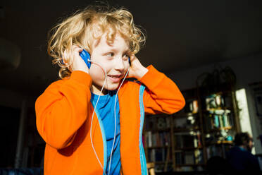 Blonder Junge schaut weg, während er zu Hause über Kopfhörer Musik hört - IHF00440