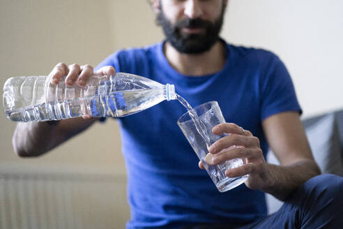 Durstiger junger Mann gießt zu Hause Wasser in ein Trinkglas - FBAF01633