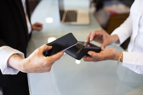 Rezeptionistin mit Kreditkartenlesegerät, während ein Kunde an der Hotelrezeption kontaktlos bezahlt - LJF02171