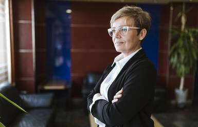 Thoughtful businesswoman looking away while standing in lobby at hotel - LJF02174