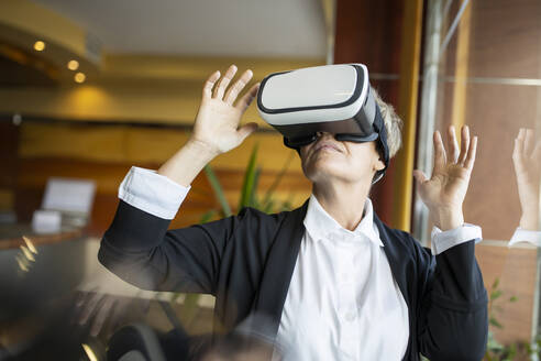 Unternehmerin gestikuliert bei der Nutzung eines Virtual-Reality-Simulators im Hotel - LJF02177
