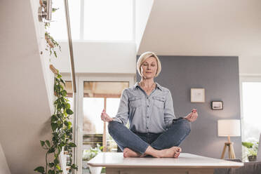 Woman sitting in lotus position on table at home - UUF23094