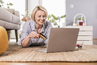 Lächelnde Frau, die beim Online-Shopping zu Hause mit ihrer Kreditkarte bezahlt - UUF23111