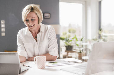 Smiling businesswoman on video call through digital tablet at home office - UUF23121