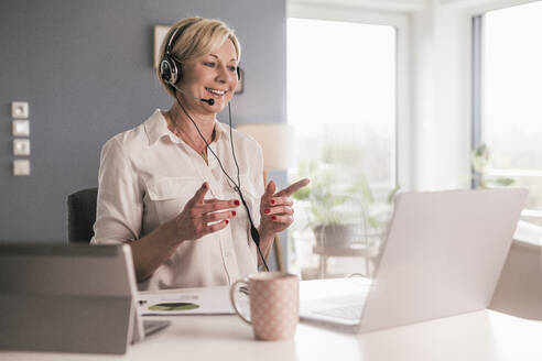 Female entrepreneur gesturing while talking on video call through laptop in home office - UUF23130