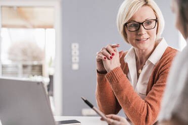 Blond businesswoman in eyeglasses looking at female coworker in home office - UUF23139