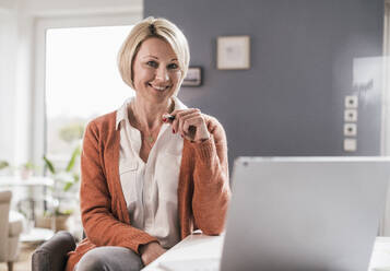 Smiling businesswoman with laptop at home office - UUF23142