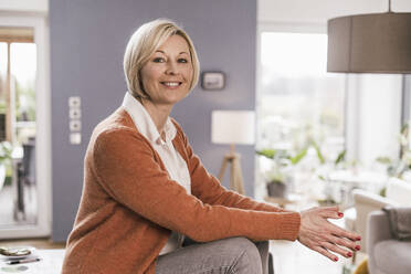 Happy blond businesswoman sitting with hands clasped in home office - UUF23151