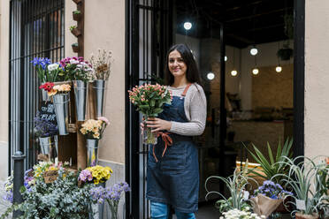 Junge Blumenhändlerin hält Blumenvase im Laden stehend - EGAF02110