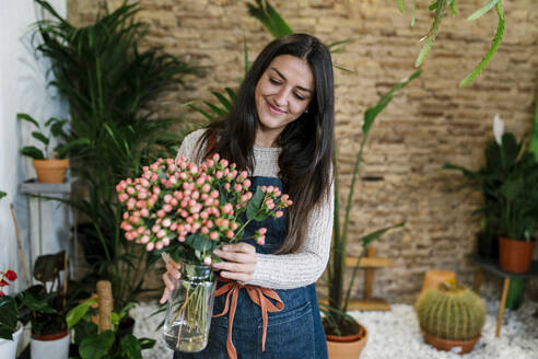 Lächelnde junge Blumenhändlerin mit Hypericum-Blumenvase im Geschäft - EGAF02113