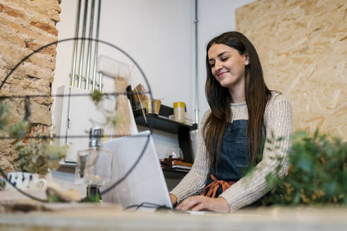 Lächelnde schöne Besitzerin mit Laptop in einem Blumenladen - EGAF02115