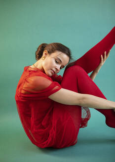 Schöne Frau, die Ballett tanzt, während sie auf türkisfarbenem Boden sitzt - AXHF00210