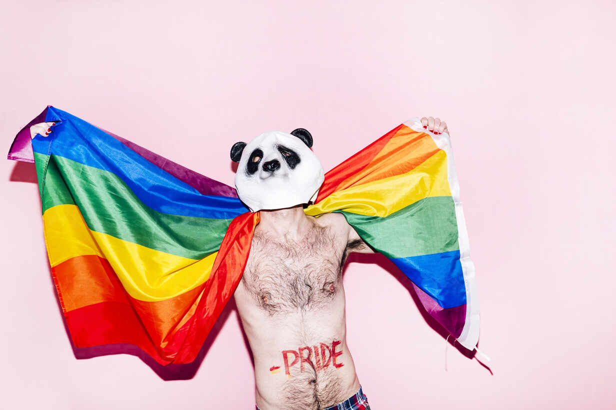 Gay man wearing Panda mask while holding rainbow flag against pink  background stock photo