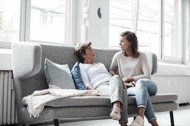 Relaxed senior woman talking with granddaughter while sitting on sofa at home - GUSF05494