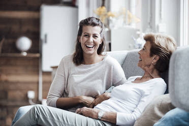 Lachende Frau, die mit ihrer Großmutter auf dem Sofa zu Hause sitzt - GUSF05497