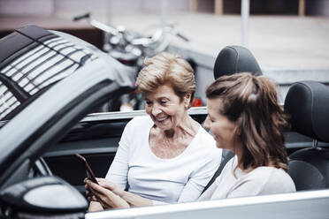 Junge Frau, die im Auto sitzend von ihrer Großmutter ein Mobiltelefon benutzt - GUSF05502