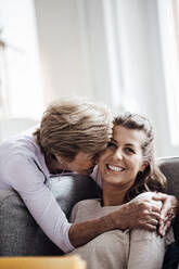 Loving grandmother embracing smiling woman while sitting on sofa at home - GUSF05532