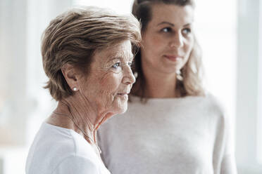 Senior woman looking away while standing by granddaughter at home - GUSF05537