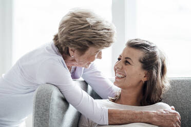 Caring grandmother looking at granddaughter while embracing at sofa - GUSF05540