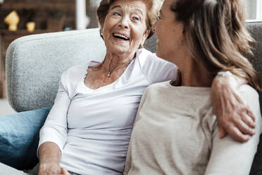 Glückliche Großmutter lacht ihre Enkelin an, während sie auf dem Sofa sitzt - GUSF05551