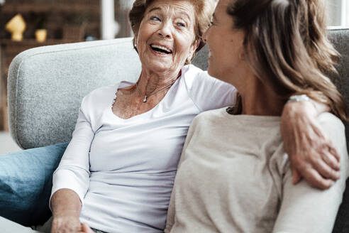 Happy grandmother laughing at granddaughter while sitting on sofa - GUSF05551