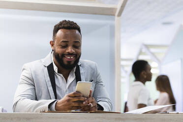 Smiling businessman using mobile phone at office - PNAF01086