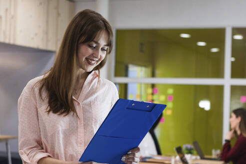 Young businesswoman reading clipboard file in office - PNAF01123