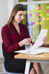 Junge Geschäftsfrau, die bei der Arbeit im Büro ein Dokument analysiert - PNAF01175